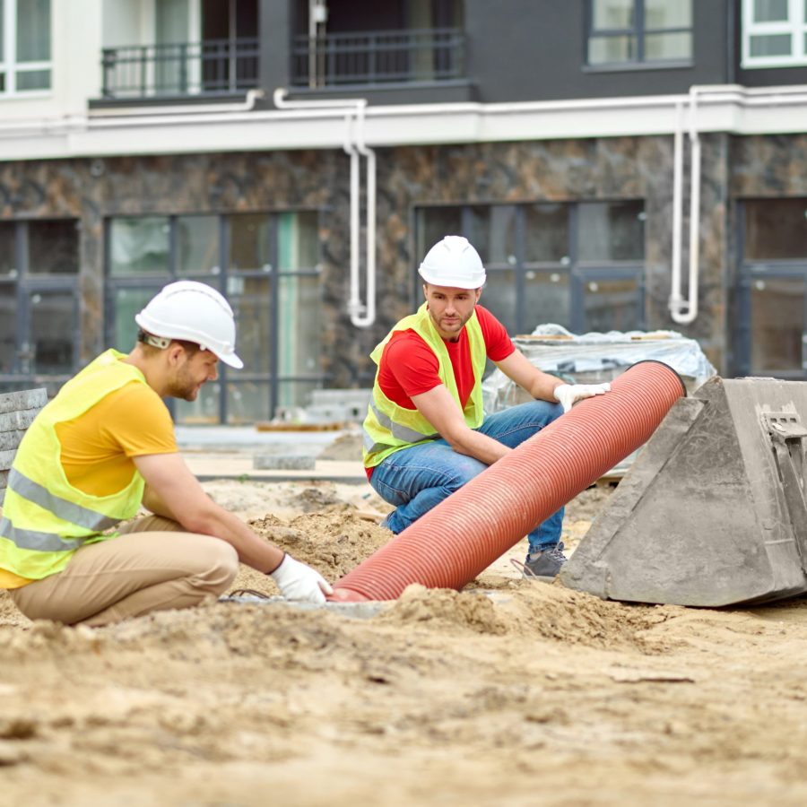 two men crouched near pipe at construction site